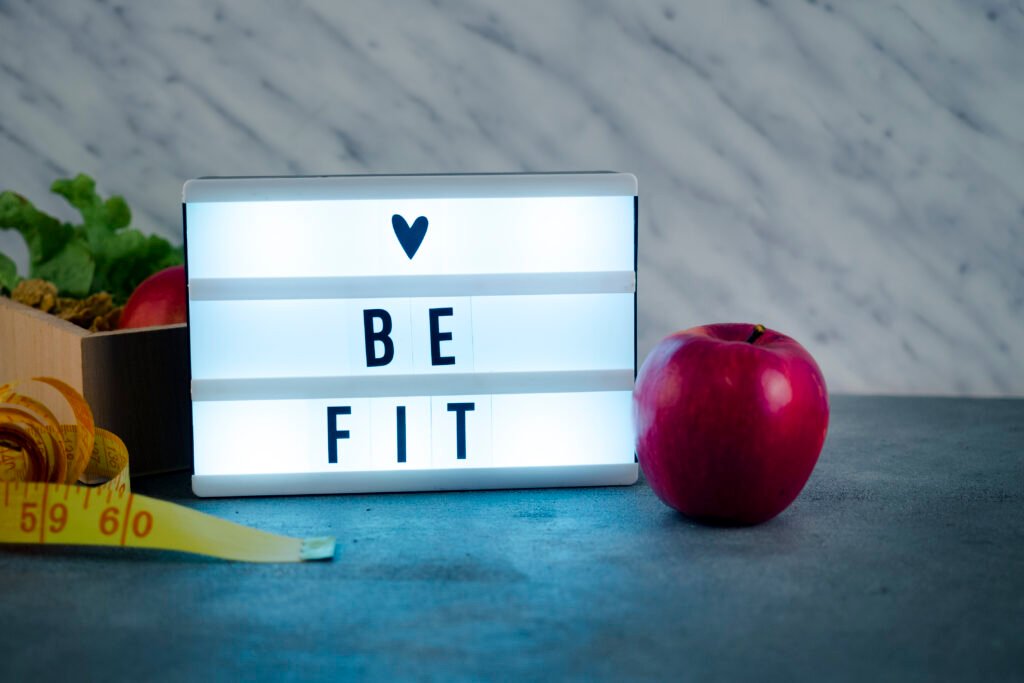 Light box with 'Be Fit' message beside an apple and measuring tape