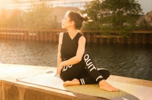 a woman sitting on a yoga mat by water